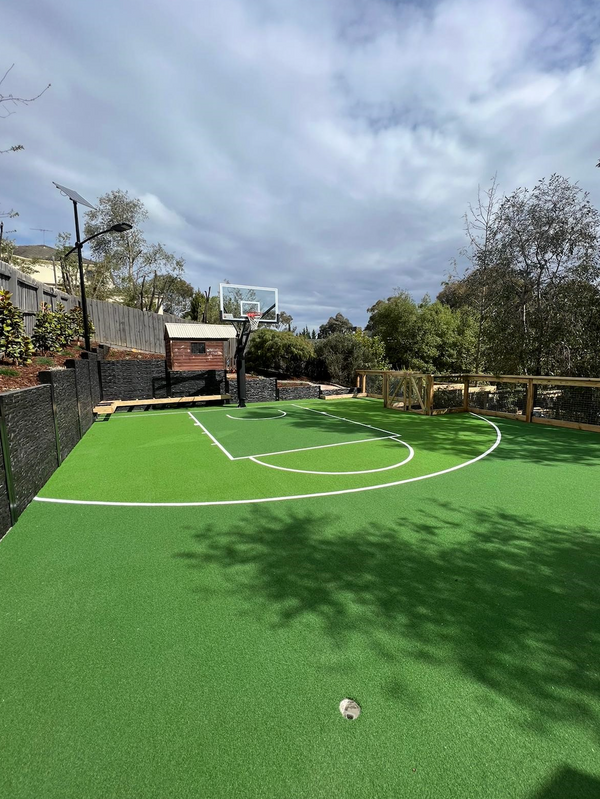 Outdoor synthetic turf basketball court with hoop in a landscaped backyard setting