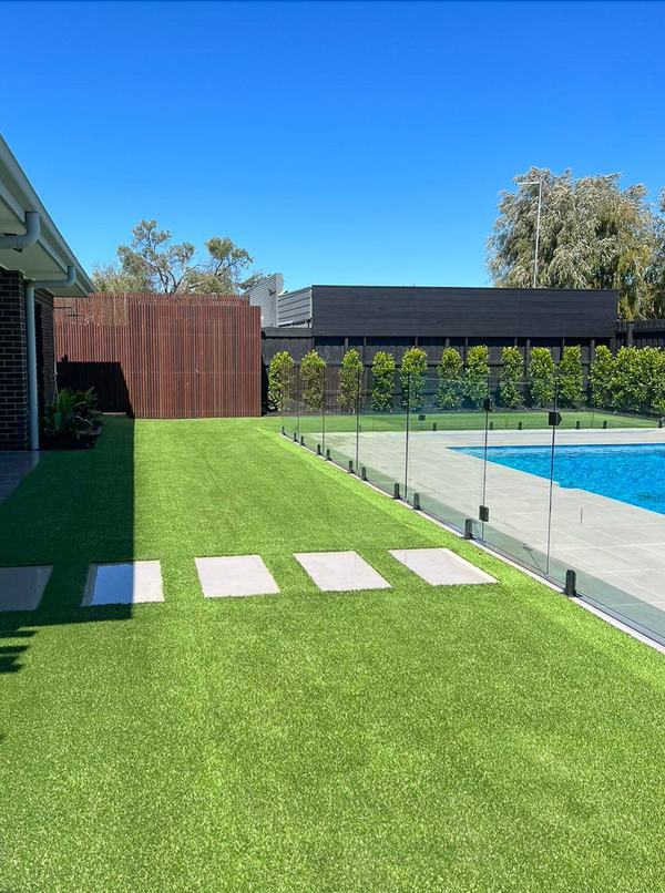 Artificial grass backyard with stepping stones next to a glass-fenced swimming pool