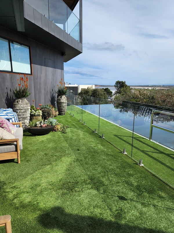 Modern balcony with synthetic grass, glass railing, outdoor seating, and garden planters
