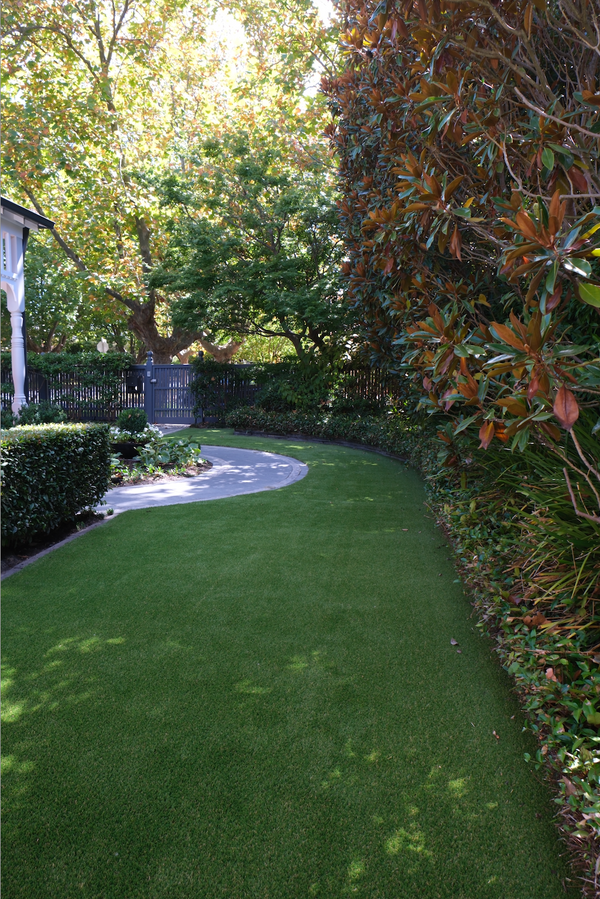 Lush synthetic grass lawn in a residential garden with bushes and trees