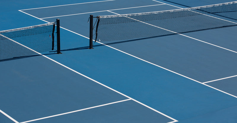 Blue acrylic tennis court with white lines and black nets, outdoor sports surface