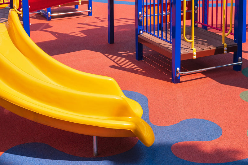 Yellow slide and colorful rubber softfall flooring at a childcare playground