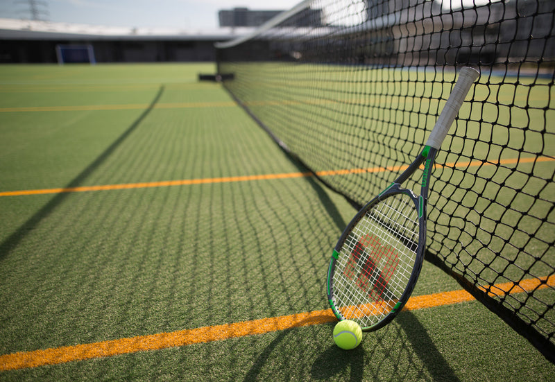 Synthetic turf tennis court with tennis racket and ball by the net