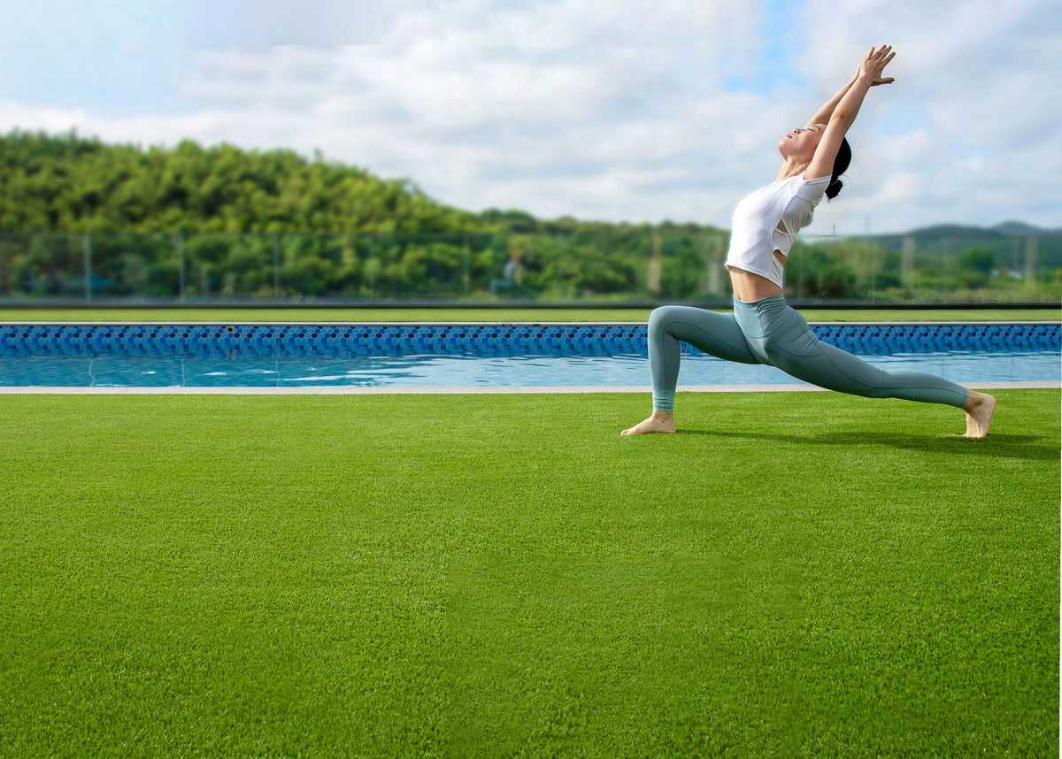 Woman doing yoga pose on synthetic turf near outdoor pool with trees in background