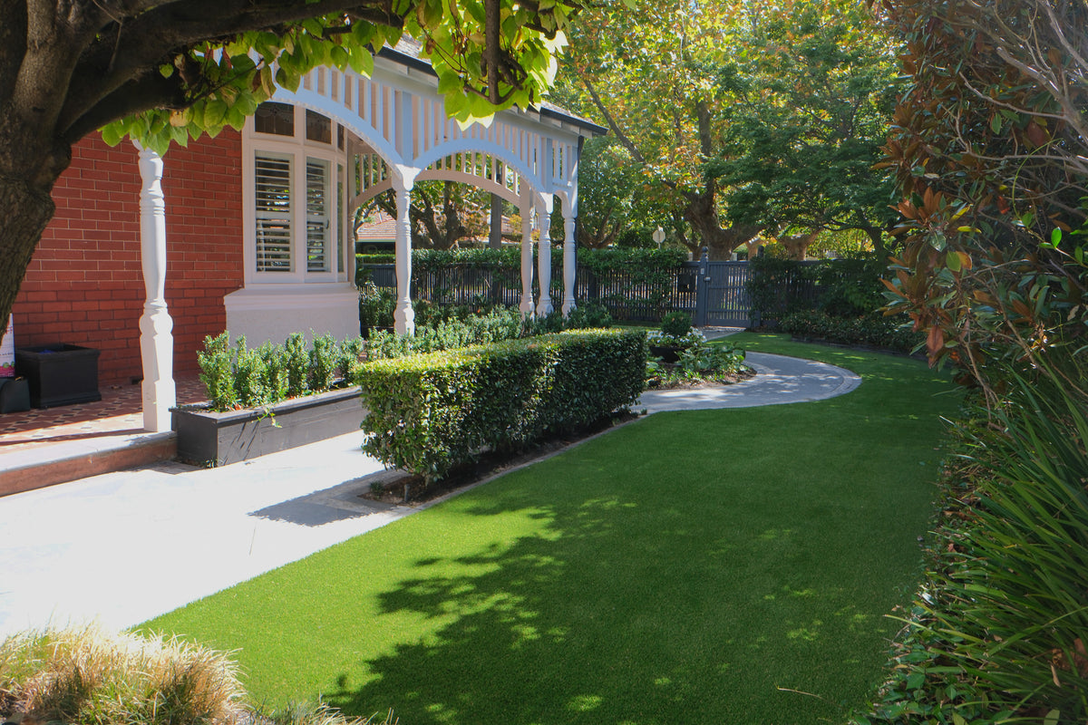 Lush synthetic grass backyard with modern landscaping and garden path by a brick house