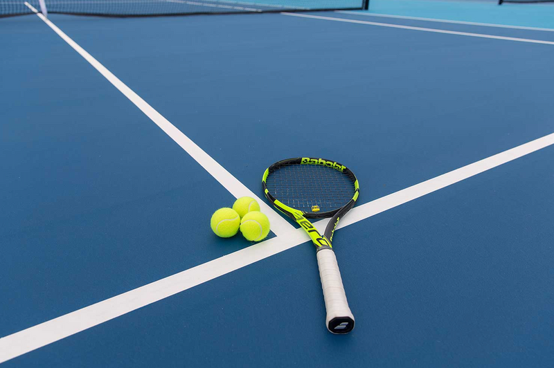 Blue acrylic tennis court with white lines, tennis racquet and three yellow balls