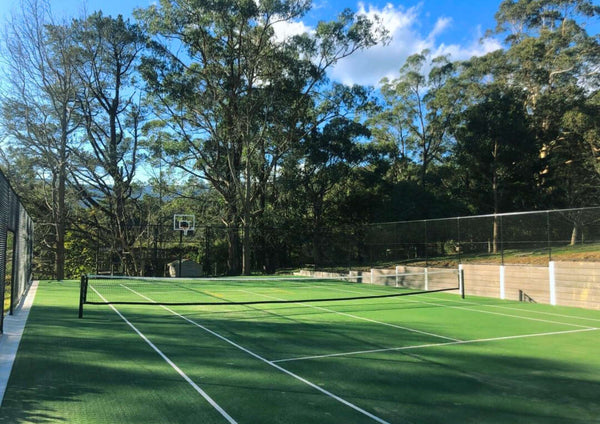 Outdoor synthetic turf tennis court installation surrounded by fencing and trees