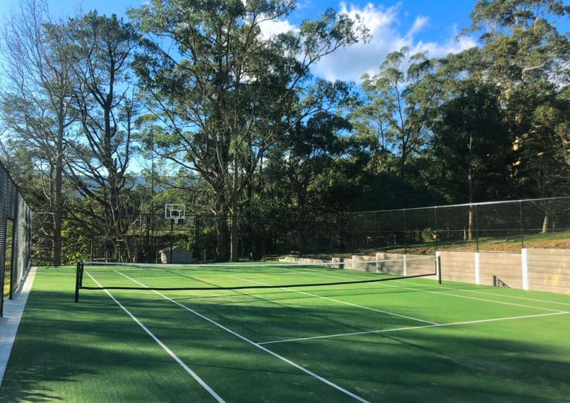 Outdoor synthetic turf tennis court installation surrounded by fencing and trees