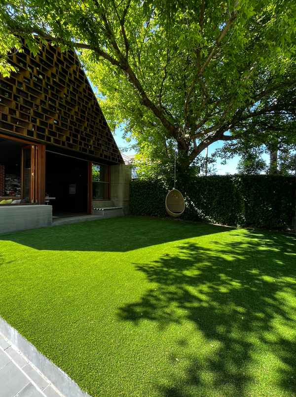 Modern backyard with synthetic turf lawn, large tree, hanging chair, and unique house façade
