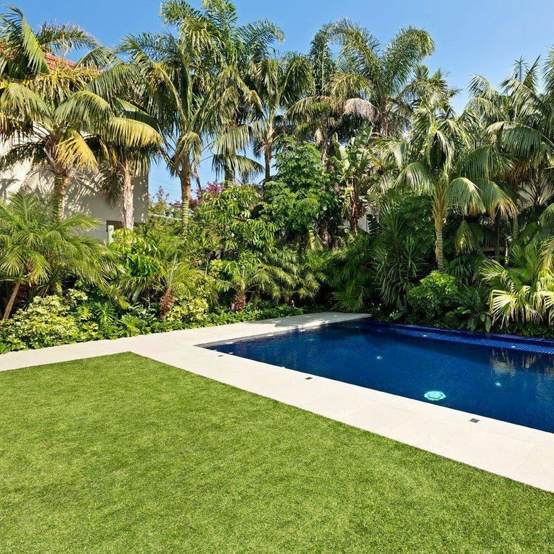 Synthetic grass lawn beside a backyard pool with tropical landscaping